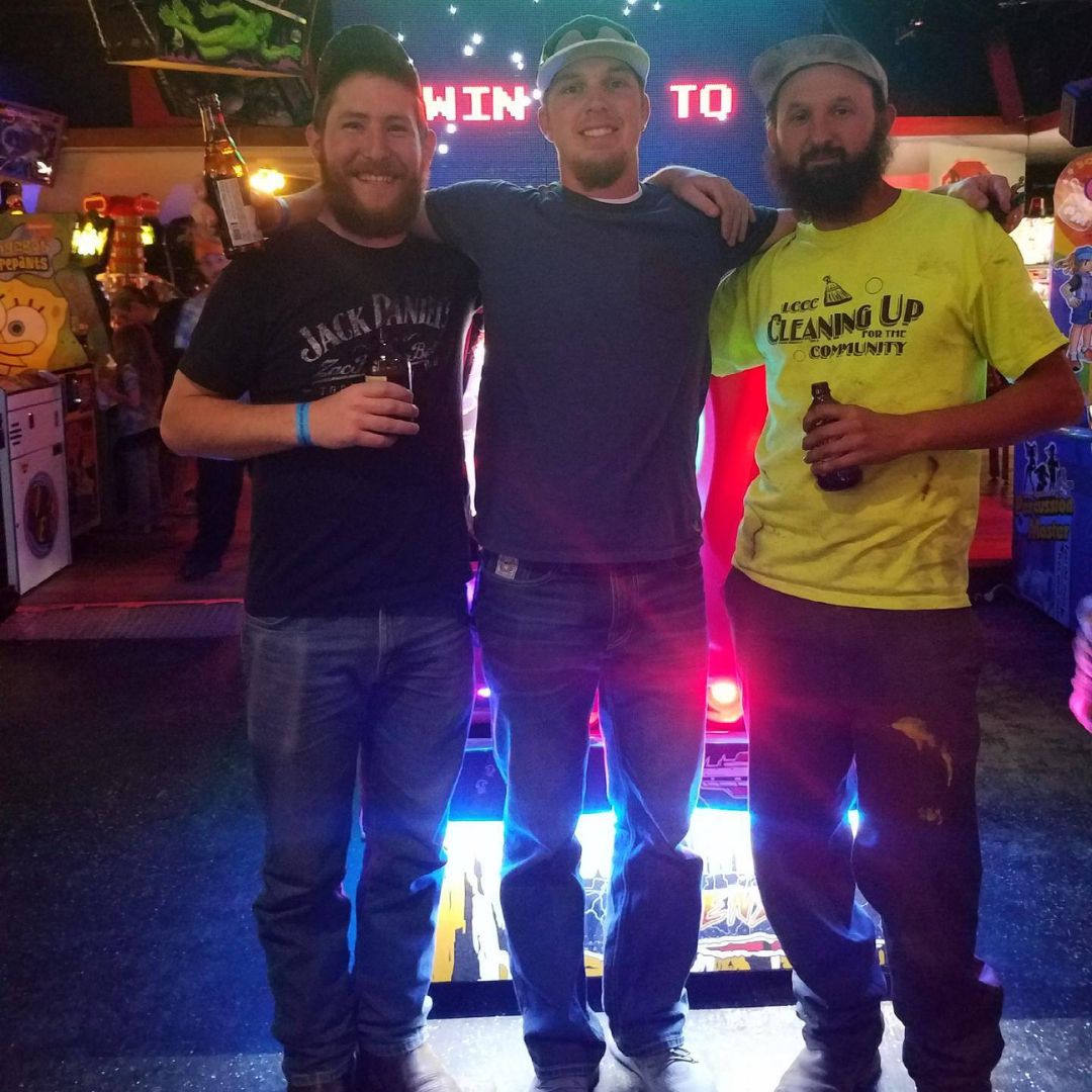 Three men standing next to each other in an arcade. 